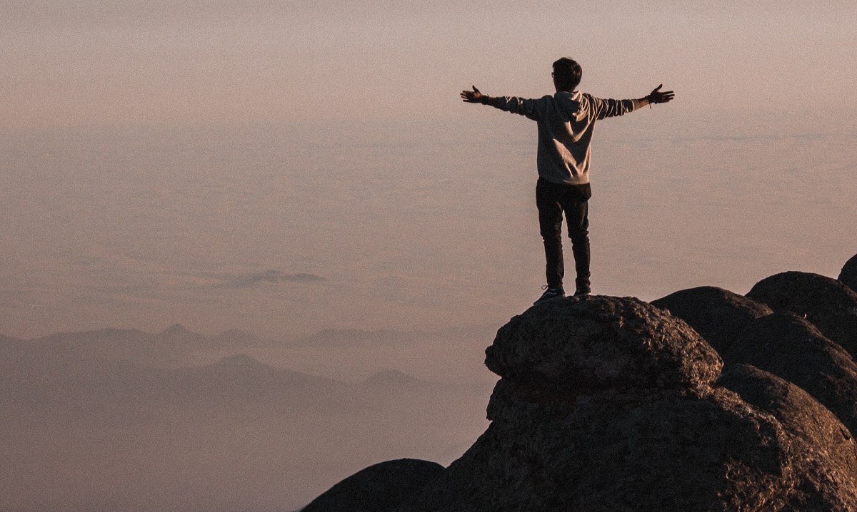 Man with open arms on top of a mountain